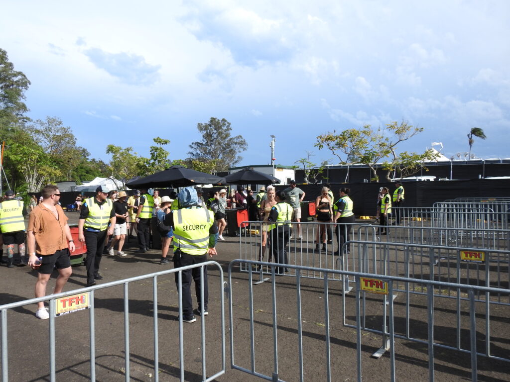 Crowd control staff in yellow SECURITY vests managing festival ingress at barriers